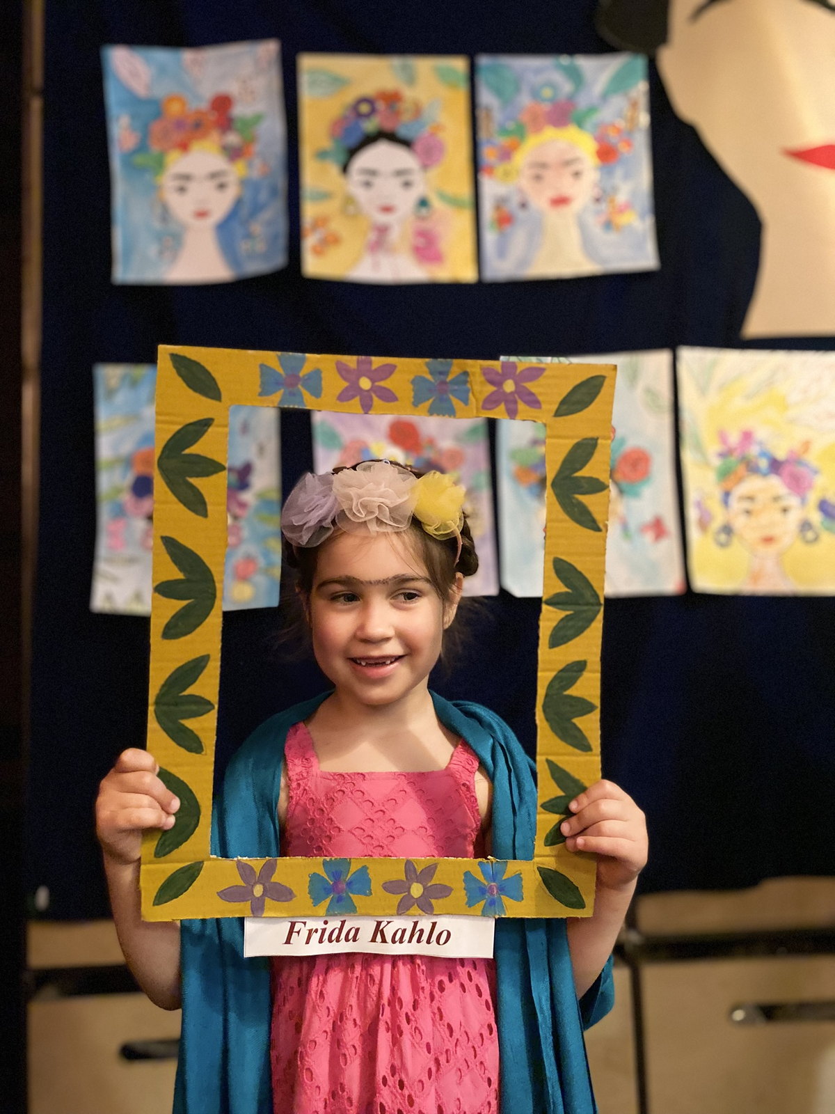 Дівчинка в образі Фріди Кало з квітами у волоссі тримає рамку «Frida Kahlo»