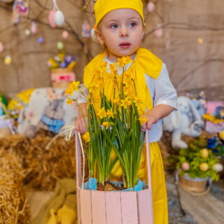 Хлопчик у костюмі курчати тримає кошик із нарцисами на великодній фотозоні